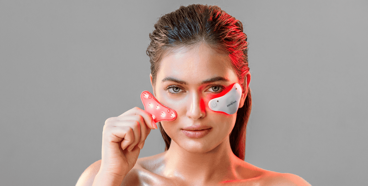 Woman using GloTech Minis LED light therapy device under the eye while holding a second device—showing targeted red and infrared light treatment for wrinkles, puffiness, and dark circles.