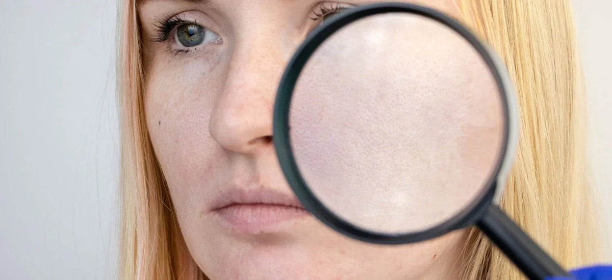 Close-up of a woman examining her skin pores with a magnifying glass.