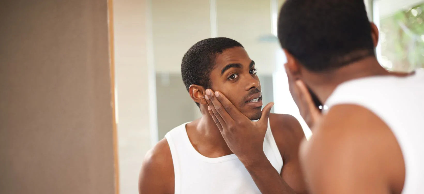 Man examining skin in mirror, skincare routine, LED therapy benefits for men's skin care