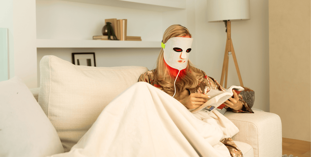 Woman relaxing on the sofa wearing the Glotech Mask Pro red light therapy mask, illustrating an easy at-home, dermatologist-recommended LED routine used several times per week for face and neck.