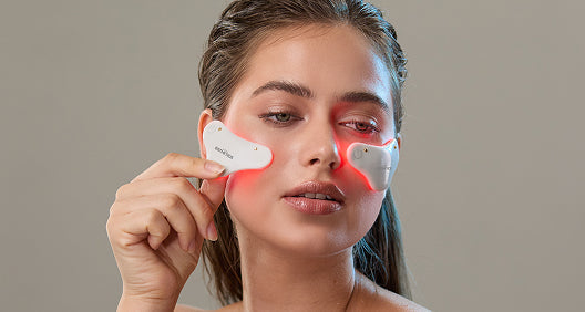 Woman using Glotech Minis LED device—targeted red, infrared, and yellow light therapy for reducing wrinkles, dark circles, puffiness, and fine lines under the eyes.