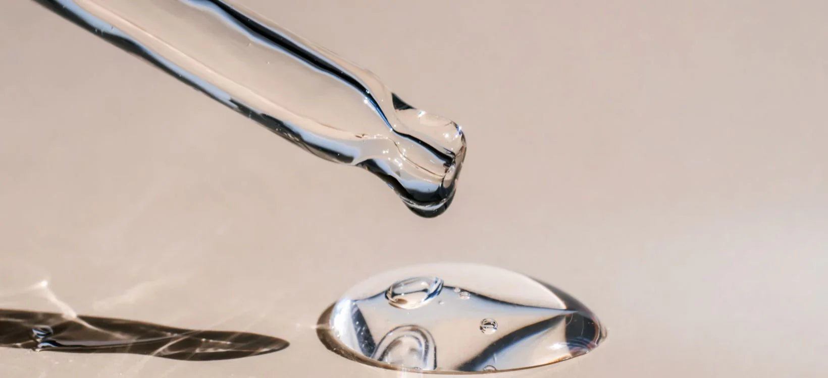 Close-up of a dropper releasing a clear liquid serum on a smooth surface, representing skincare serum application.